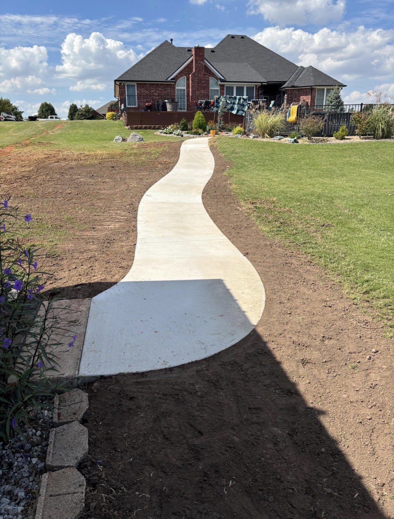 Curved poured concrete walkway leading up to a brick home